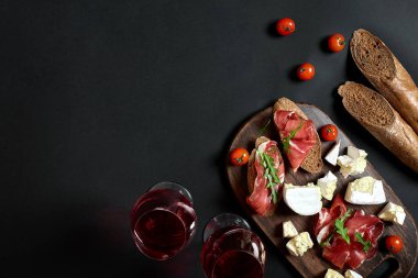 Jambon, salam, baget dilimleri, domates ve nutson rustik ahşap masa, iki bardak siyah arka plan üzerinde kırmızı şarap