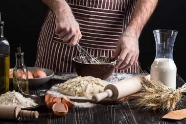 Erkek Şef ekmek ahşap masa üzerinde yumurta kırbaçlanan. Pişirme Unlu Mamüller veya hamur için malzemeler
