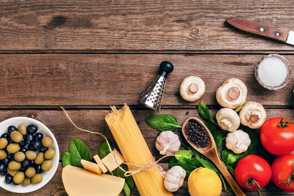 stock image Pasta ingredients - tomatoes, olive oil, garlic, italian herbs, fresh basil, salt and spaghetti on a wooden background with copy space, horizontal, top view