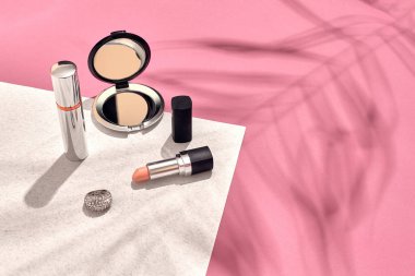 Şık kadın kozmetik ve aksesuarları. Düz yatıyordu. Pembe ve beyaz arka plan. Bir palmiye yaprak gölge