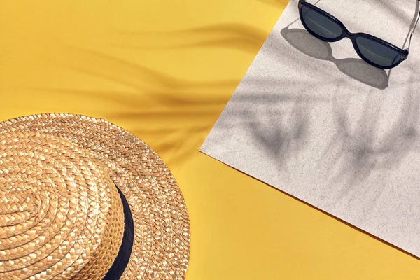 Straw beach womans hat and sun glasses, top view yellow and white paper background with shadow from a palm leaf. — Stock Photo, Image