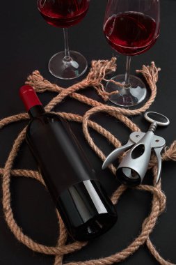 Kırmızı şarap şişesi, iki gözlük ve tirbuşon siyah arka plan üzerine. Kopya alanı ile üstten görünüm