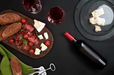 Kırmızı şarap, peynir, kiraz domates, ekmek ve prosciutto ahşap üzerinde kurulu siyah zemin, üstten görünüm, kopya alanı üzerinde