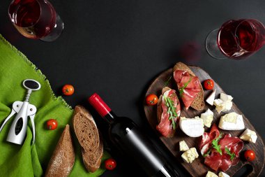 Jambon, salam, baget dilimleri, domates ve nutson rustik ahşap masa, iki bardak siyah arka plan üzerinde kırmızı şarap
