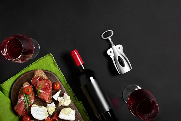 Jambon, salam, baget dilimleri, domates ve nutson rustik ahşap masa, iki bardak siyah arka plan üzerinde kırmızı şarap — Stok fotoğraf