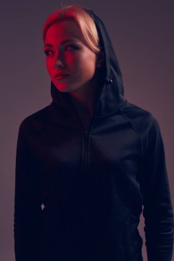 Koyu arka plan üzerinde siyah kukuleta ve şort giyen genç güzel kadın