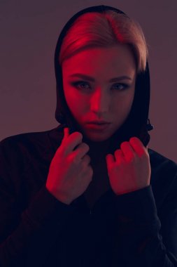 Koyu arka plan üzerinde siyah kukuleta ve şort giyen genç güzel kadın. Portre