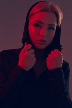 Koyu arka plan üzerinde siyah kukuleta ve şort giyen genç güzel kadın. Portre