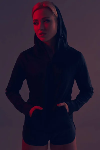 Belle fille sportive séduisante avec la silhouette sexy mince dans le sweat à capuche noir, sous-vêtements de sport et petit short noir pose en studio — Photo