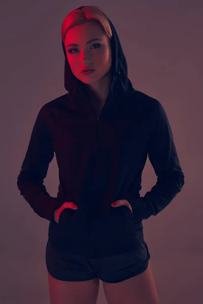Mooie verleidelijke sportieve meisje met de slanke sexy figuur in de zwarte hoodie, sport ondergoed en kleine zwarte shorts is poseren in de studio — Stockfoto