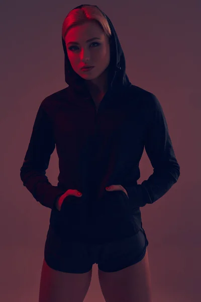 Vackra förförisk sportig tjej med den slank sexig figuren i svart hoodie, sport underkläder och lite svarta shorts poserar i studion — Stockfoto