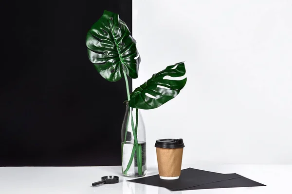 Forró kávé barna papír poharat és a zöld levelek üvegben, hogy asztalra a háttér fekete-fehér fal — Stock Fotó