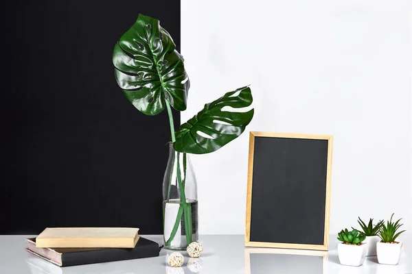El elegante interior con marco de póster simulada, hojas en botella de vidrio en la mesa con la pared en blanco y negro en el fondo . — Foto de Stock