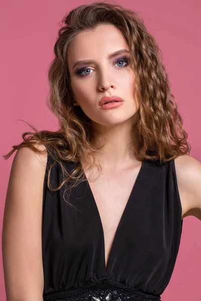 Gyönyörű divatos lány hosszú göndör haja egy fekete ruhás, a stúdióban, a rózsaszín háttér. — Stock Fotó