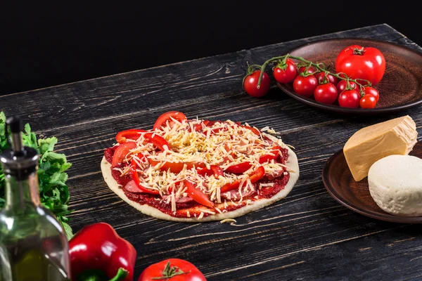 Ωμή ζύμη για πίτσα προετοιμασία με συστατικό: σάλτσα ντομάτας, μοτσαρέλα, ντομάτα, βασιλικό, ελαιόλαδο, τυριά, μπαχαρικά, σερβίρεται στη ρουστίκ ξύλινο τραπέζι. — Φωτογραφία Αρχείου