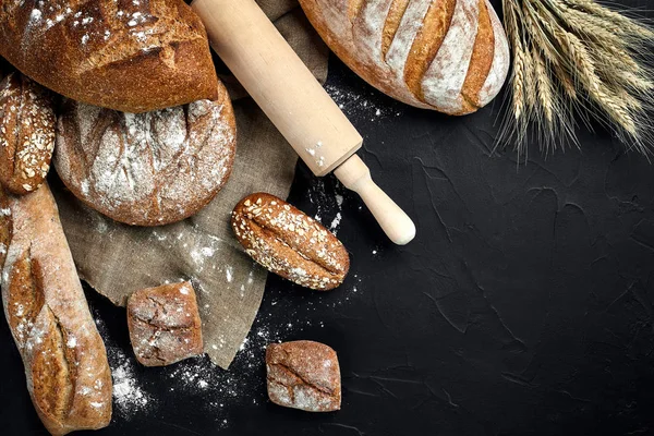 Panificio - oro rustico croccante pagnotte di pane e focacce su fondo lavagna nera . — Foto Stock