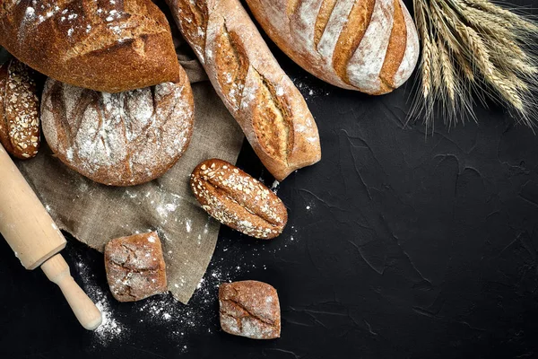 Panificio - oro rustico croccante pagnotte di pane e focacce su fondo lavagna nera . — Foto Stock