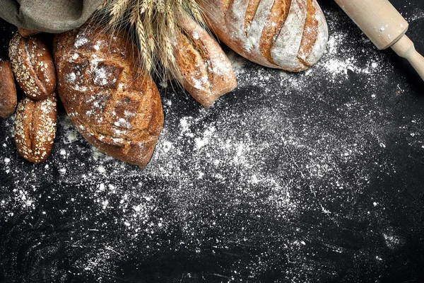Domowy chleb żytni posypany mąką i różnych ziarna i nasiona na czarnym tle z silnie pszenicy i żyta i owsa. — Zdjęcie stockowe