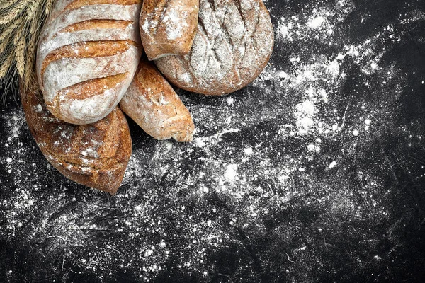 Domowy chleb żytni posypany mąką i różnych ziarna i nasiona na czarnym tle z silnie pszenicy i żyta i owsa. — Zdjęcie stockowe