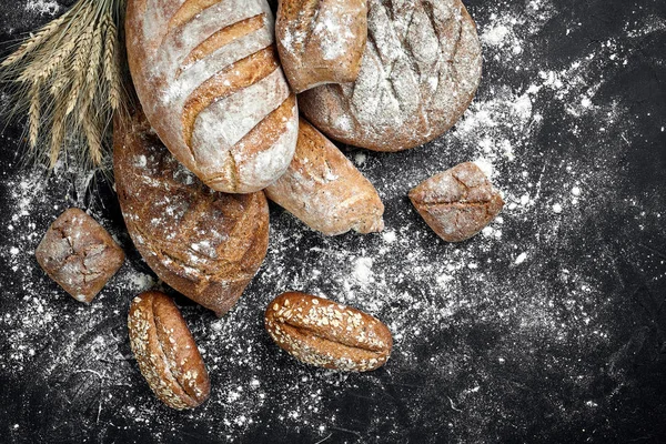 Pâine de secară de casă presărată cu făină și diverse cereale și semințe pe un fundal negru cu spikelets de grâu sau secară și ovăz . — Fotografie, imagine de stoc