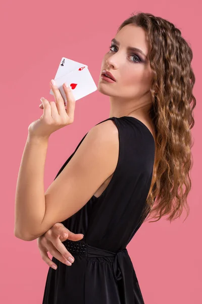 Молодая женщина держит два туза в руке на розовом фоне — стоковое фото
