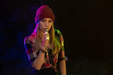 Vaping kız. Genç hipster kadın vape e-cig siyah arka plan üzerine. Hip-hop tarzı. Stüdyo vurdu