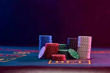 Oyun masasının mavi kapağında duran renkli çipler. Siyah arka plan. Kumar eğlencesi, poker, kumarhane konsepti. Yakın plan..
