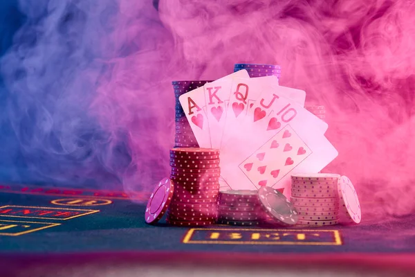 Winning combination in poker leaning on colored chips piles on blue cover of playing table. Black, smoke background, red and blue backlights. Casino. — Stock Photo, Image