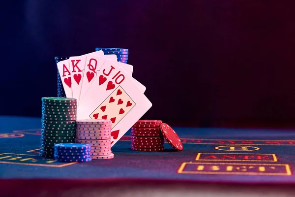 Winning combination in poker standing leaning on multicolored chips piles on blue cover of playing table. Black background. Casino concept. Close-up. — Stock Photo, Image