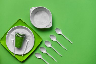 Yeşil arkaplanda fotokopi alanı olan renkli plastik tek kullanımlık sofra takımı. Piknik aleti kavramı. Üst Manzara. Seçici odaklanma. Yakın plan..
