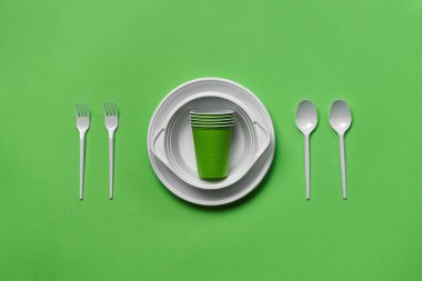 Yeşil arkaplanda fotokopi alanı olan renkli plastik tek kullanımlık sofra takımı. Piknik aleti kavramı. Üst Manzara. Seçici odaklanma. Yakın plan..