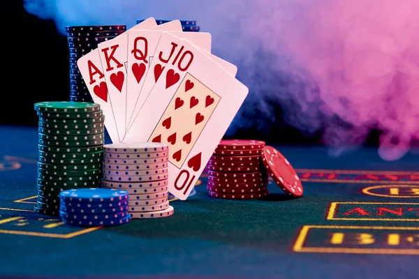 Winnende combinatie in poker leunen op gekleurde chips palen op blauwe cover van het spelen van tafel. Zwart, rookachtergrond, rode en blauwe achtergrondverlichting. Het casino. — Stockfoto
