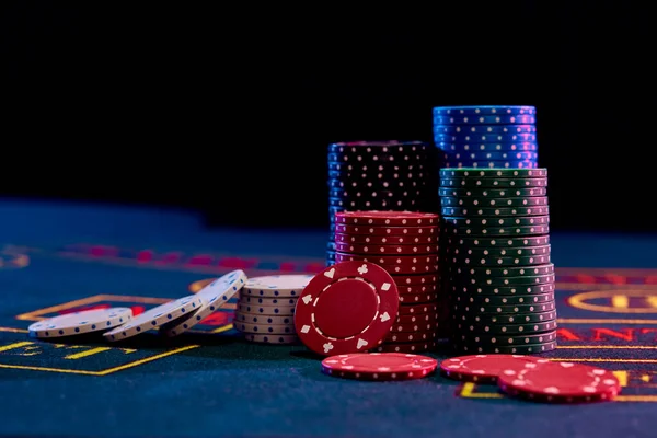 Las fichas coloridas se montan sobre la cubierta azul de la mesa de juego. Fondos negros. Juego de entretenimiento, poker, concepto de casino. Cierre. — Foto de Stock