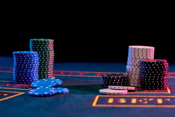 Kleurrijke chips stapels staan op de blauwe cover van het spelen van tafel. Zwarte achtergrond. Gokken entertainment, poker, casino concept. Close-up. — Stockfoto