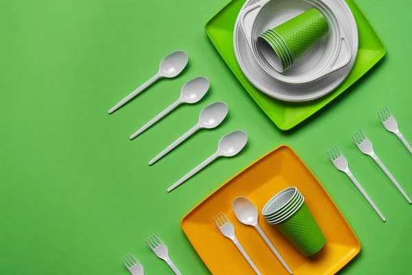 Colorful plastic disposable tableware on green background with copy space. The concept of picnic utensil. Top view. Selective focus. Close-up. — Stock Photo, Image