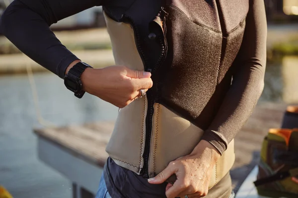 La mujer de color gris turtleneck se masturba su chaleco deportivo especial mientras se coloca al margen en un muelle de la zona costera con un tablero de cintura en él. Cierre. — Foto de Stock