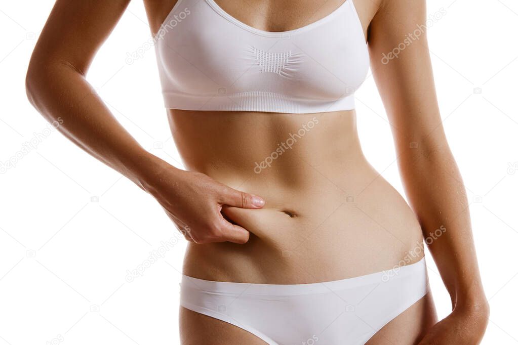 Young body of girl in white underwear, showing fat on her belly, posing isolated on white. Plastic surgery, aesthetic cosmetology concept. Close-up.