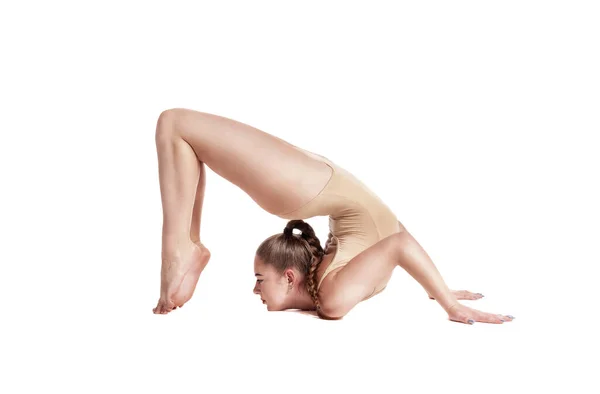 Flexible girl gymnast in beige leotard is performing complex elements of gymnastics while posing isolated on white background. Close-up. — Stock Photo, Image