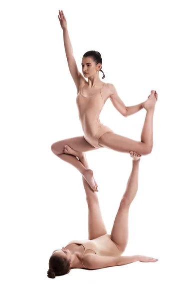 Δύο ευέλικτα κορίτσια γυμναστές σε μπεζ κολάν εκτελούν ασκήσεις ανάποδα χρησιμοποιώντας υποστήριξη και ποζάροντας απομονωμένα σε λευκό φόντο. Κοντινό πλάνο. — Φωτογραφία Αρχείου