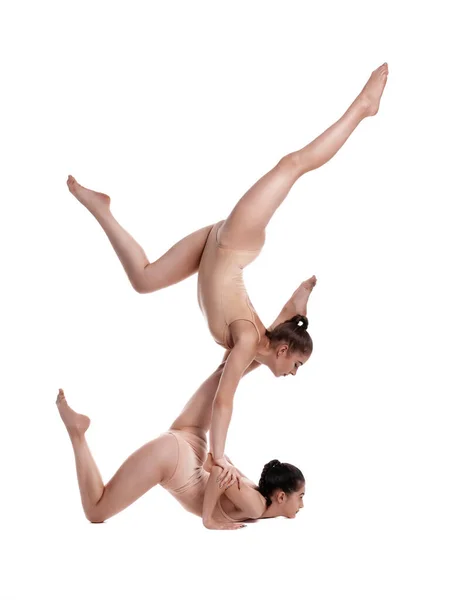 Duas meninas ginastas flexíveis em leotards bege estão realizando exercícios de cabeça para baixo usando suporte e posando isolado em fundo branco. Close-up . — Fotografia de Stock