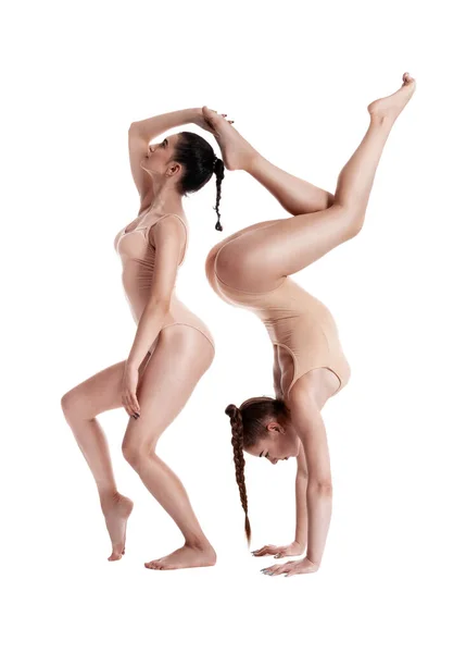 Två flexibla flickor gymnaster i beige leotards utför övningar med stöd och poserar isolerad på vit bakgrund. Närbild. — Stockfoto