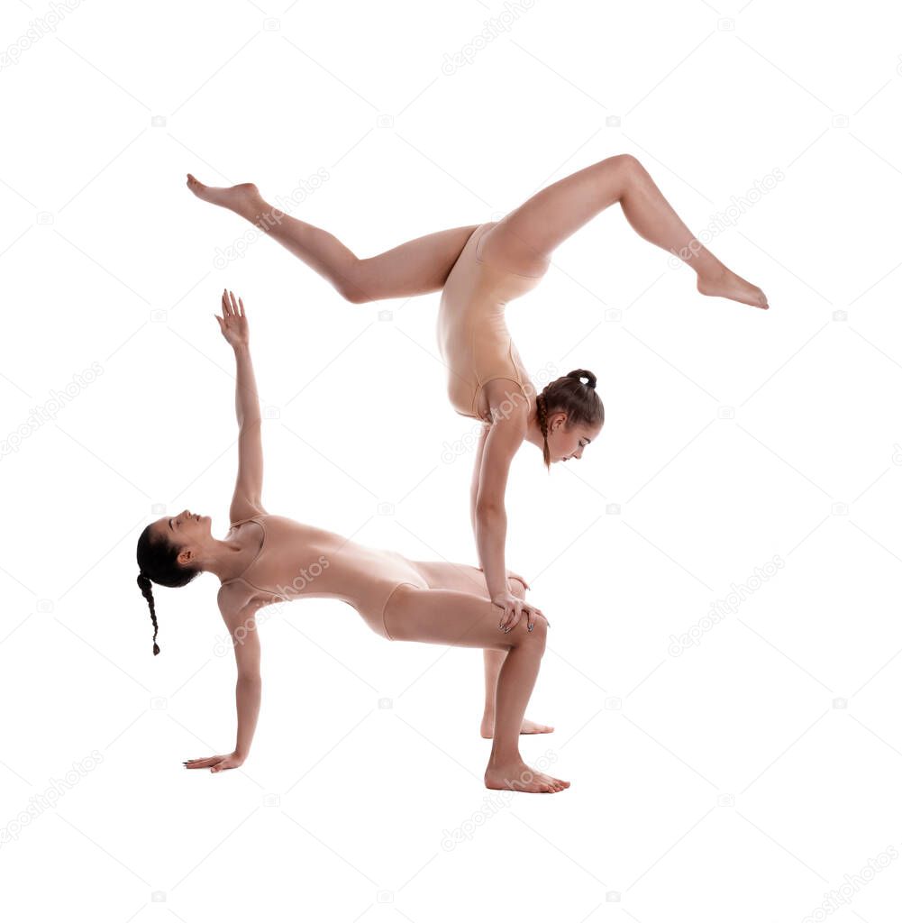Two flexible girls gymnasts in beige leotards are performing exercises upside down using support and posing isolated on white background. Close-up.