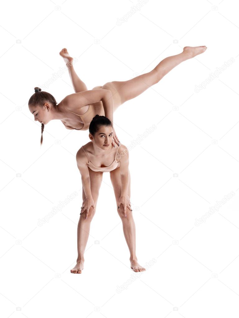 Two flexible girls gymnasts in beige leotards are performing exercises using support and posing isolated on white background. Close-up.
