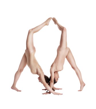 Bej taytlı iki esnek kız jimnastikçi beyaz arka planda izole edilmiş pozlar vererek destek kullanarak jimnastiğin karmaşık unsurlarını sergiliyorlar. Yakın plan..