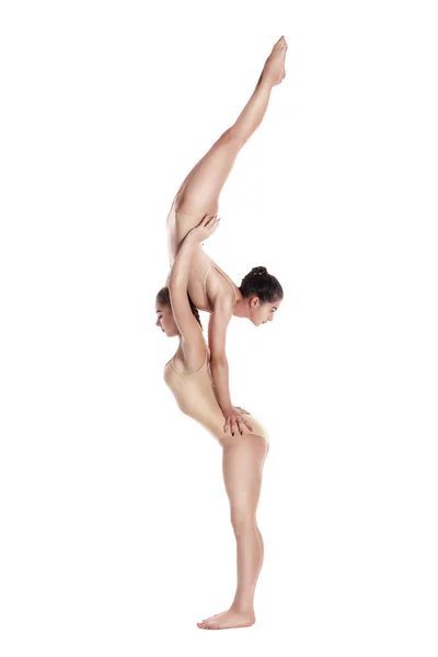 Δύο ευέλικτα κορίτσια γυμναστές σε μπεζ λεοπαρδάλεις εκτελούν ασκήσεις χρησιμοποιώντας υποστήριξη και θέτουν απομονωμένα σε λευκό φόντο. Κοντινό πλάνο. — Φωτογραφία Αρχείου