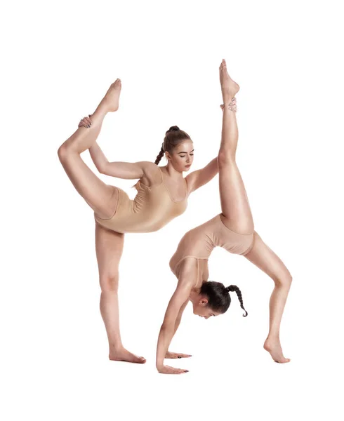 Två flexibla flickor gymnaster i beige leotards utför komplexa delar av gymnastik med hjälp av stöd, poserar isolerad på vit bakgrund. Närbild. — Stockfoto