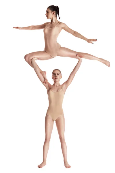 Δύο ευέλικτα κορίτσια γυμναστές σε μπεζ κολάν που εκτελούν πολύπλοκα στοιχεία της γυμναστικής χρησιμοποιώντας υποστήριξη, ποζάροντας απομονωμένα σε λευκό φόντο. Κοντινό πλάνο. — Φωτογραφία Αρχείου