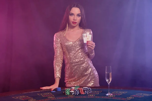 Mujer en vestido dorado mostrando cartas, posando en la mesa de juego en el casino. Negro, fondo de humo con retroiluminación de colores. Juego, póquer. Primer plano . —  Fotos de Stock