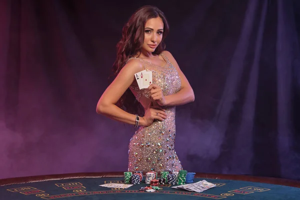 Girl playing poker, casino. Showing cards, posing at table with stacks of chips and money. Black, smoke background, colorful backlights. Close-up. — Stock Photo, Image