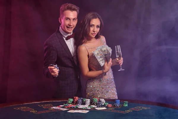 Guy está teniendo cartas, jugando al póquer en el casino, en la mesa con montones de fichas en ella. Celebra ganar con la mujer. Fondos negros de humo. Cierre. — Foto de Stock